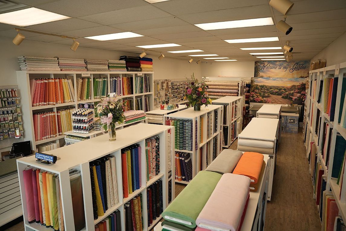 Fabric store interior with rows of colorful fabric bolts and cutting tables under bright ceiling lights