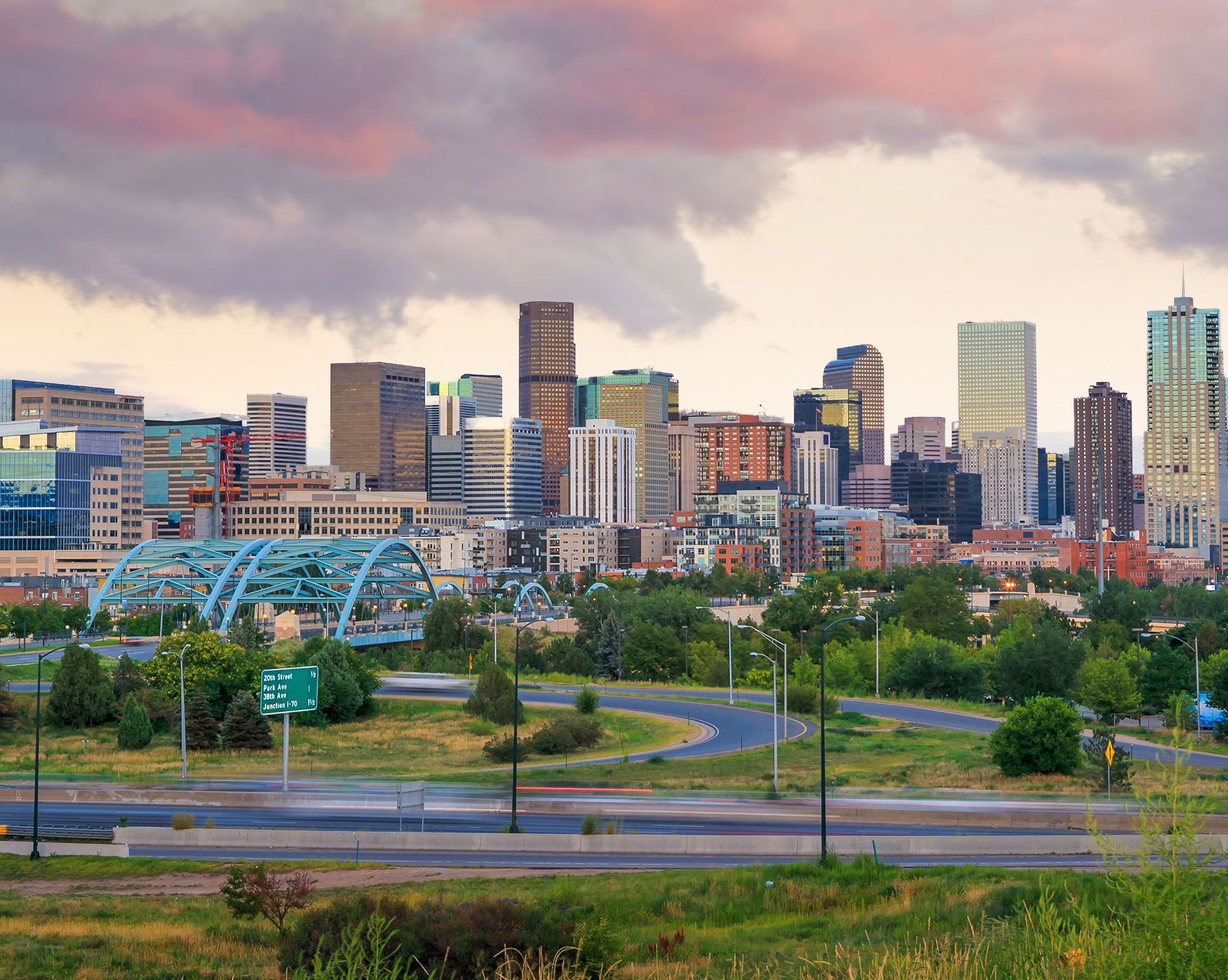 Denver skyline at dusk, with a variety of high-rise buildings under a pink and purple cloudy sky.