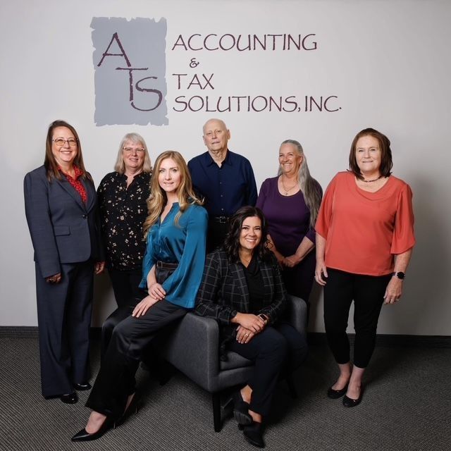 Group of seven people from ATS Accounting & Tax Solutions posing in front of their logo, with a neutral background.