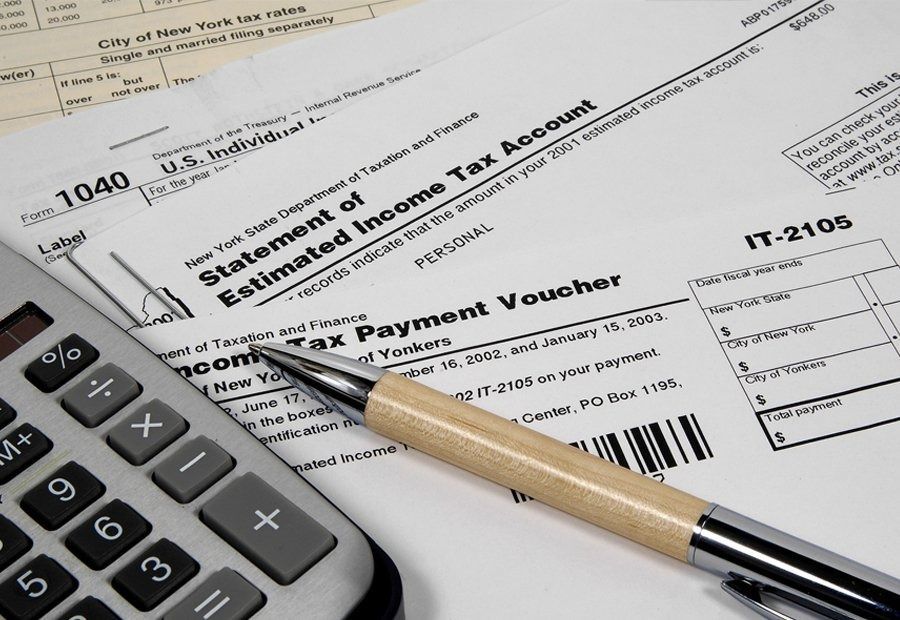 Tax forms, a calculator, and a pen on a desk, suggesting tax preparation. Includes a New York State Estimated Income Tax form.