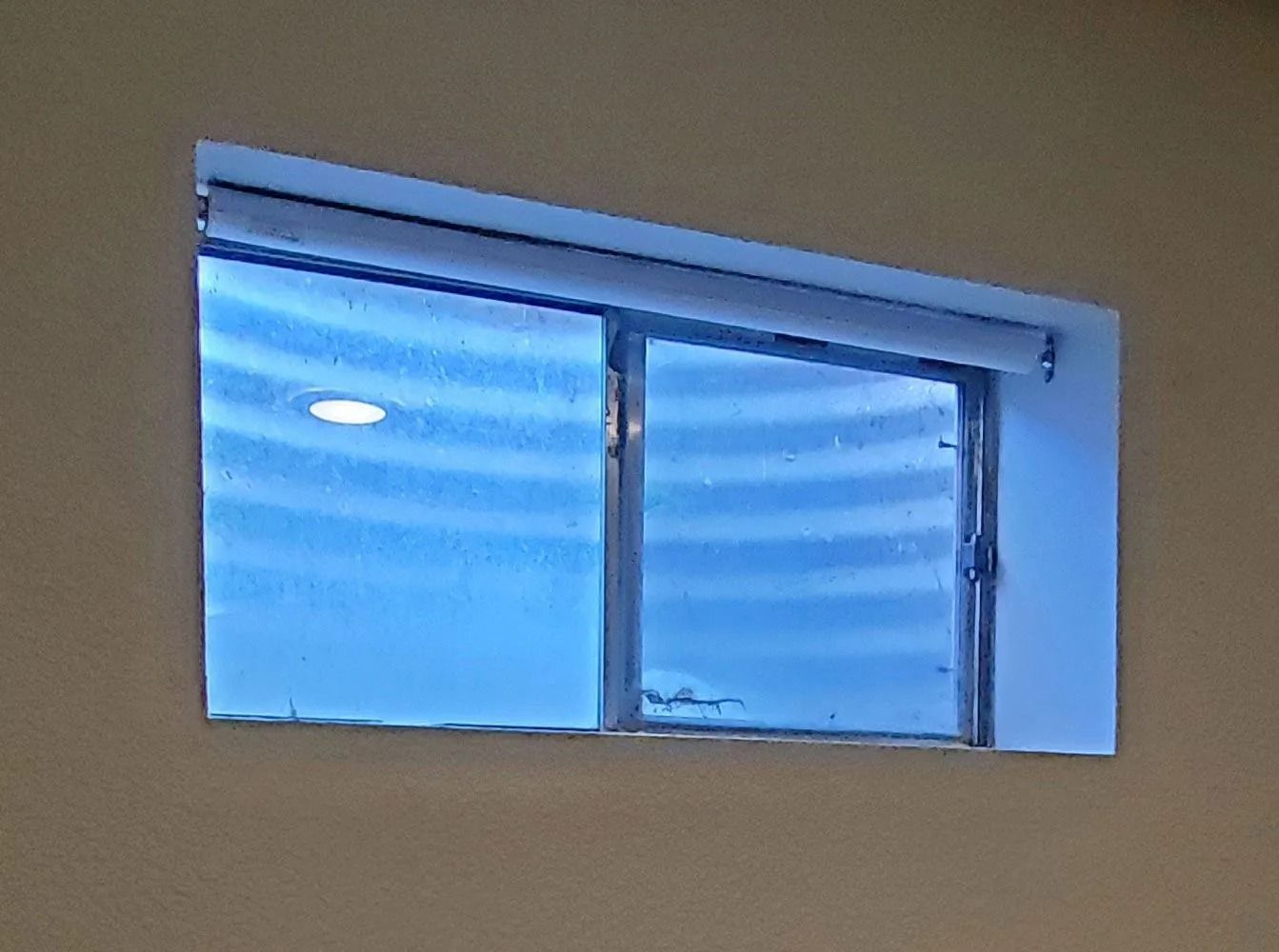 A rectangular window with a blue view, set in a tan wall. The window has a light inside.