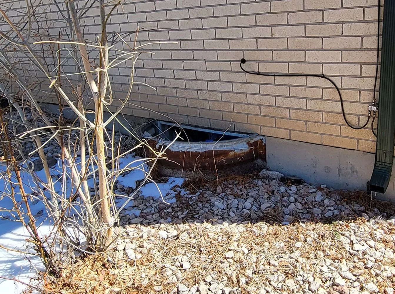 A brick building with a damaged foundation, leaves and snow in front.