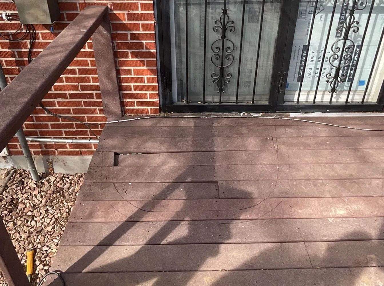 Brown composite deck with handrail next to a brick wall and a door with security bars.