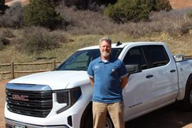 A man is standing in front of a white gmc truck.