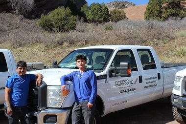 Two men are standing in front of a white truck that says emergency