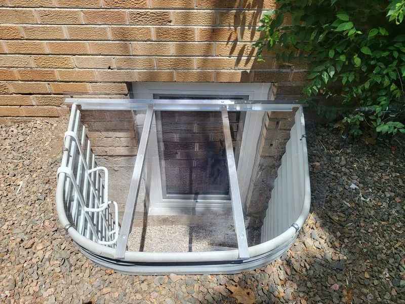 Brick building exterior with a window well and white metal window guard.