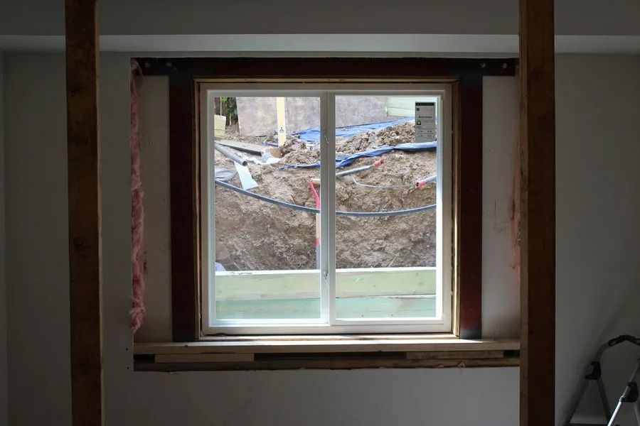 Window in a wall during construction with a dirt excavation visible outside.
