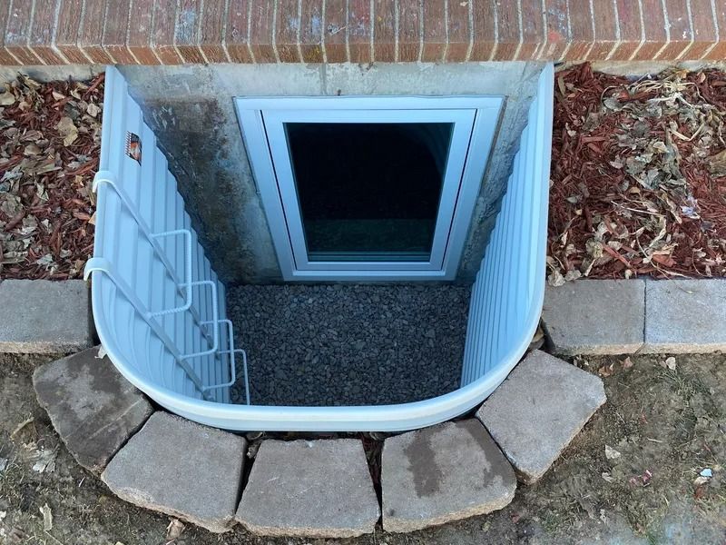 White window well with gravel, window, and metal safety bars, set in brick and concrete near ground.