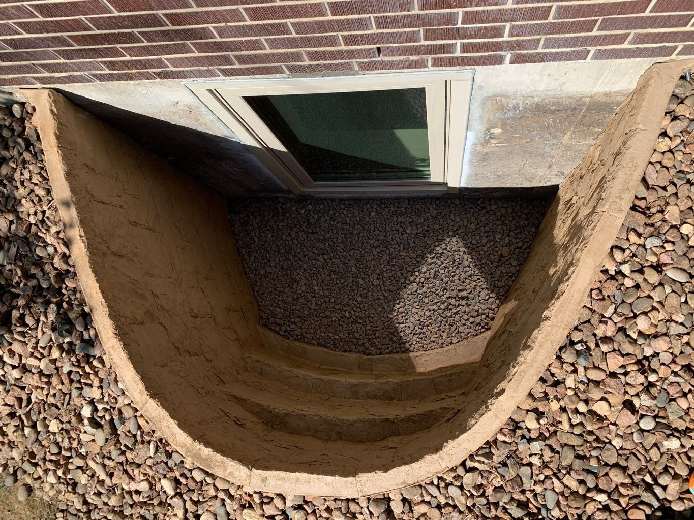 Basement window well with gravel and curved concrete walls.