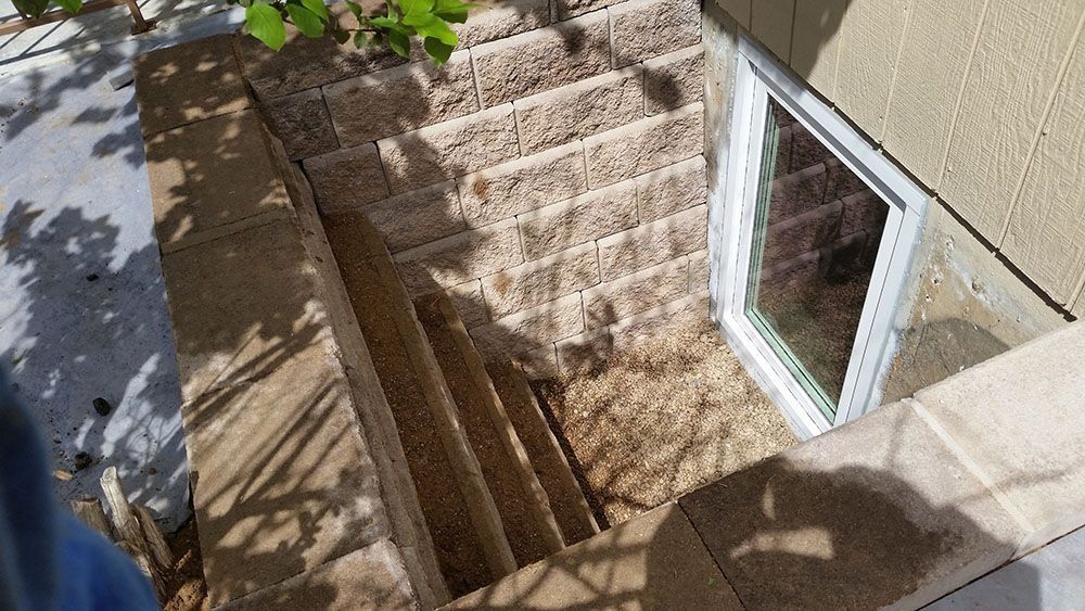 A window in a basement with stairs leading up to it.