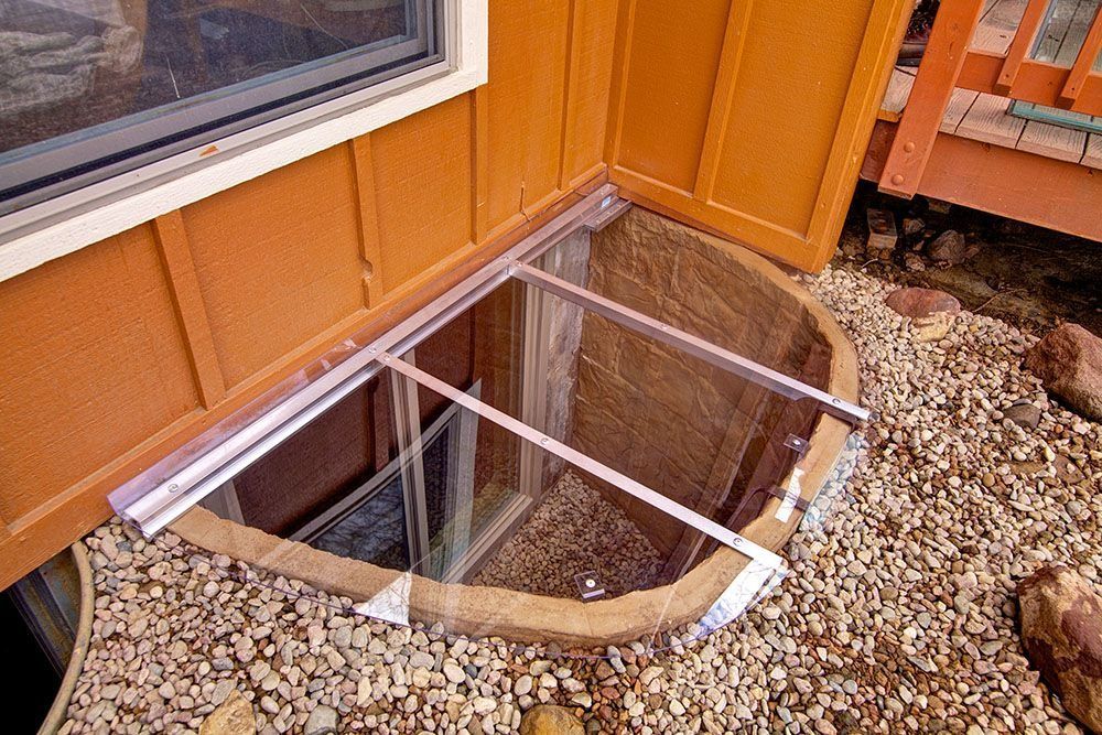 A window well with a clear cover on it is sitting next to a house.