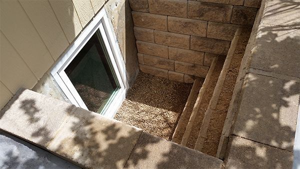 Window well with steps leading down, gravel floor, tan brick walls and a white-framed window.