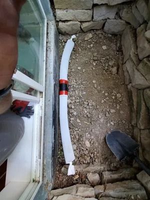 Person near window, working on drainage pipe system. Gravel and stone wall visible.