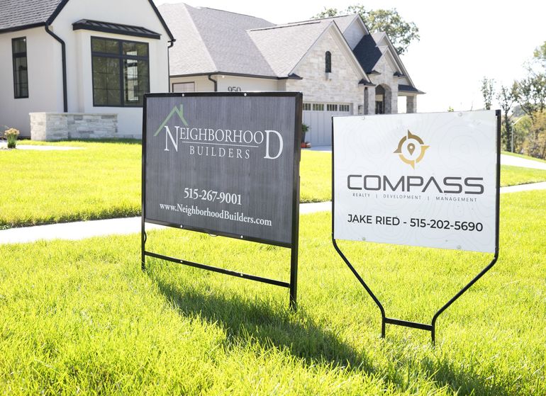 Two signs in front of a house that say Neighborhood builders and compass