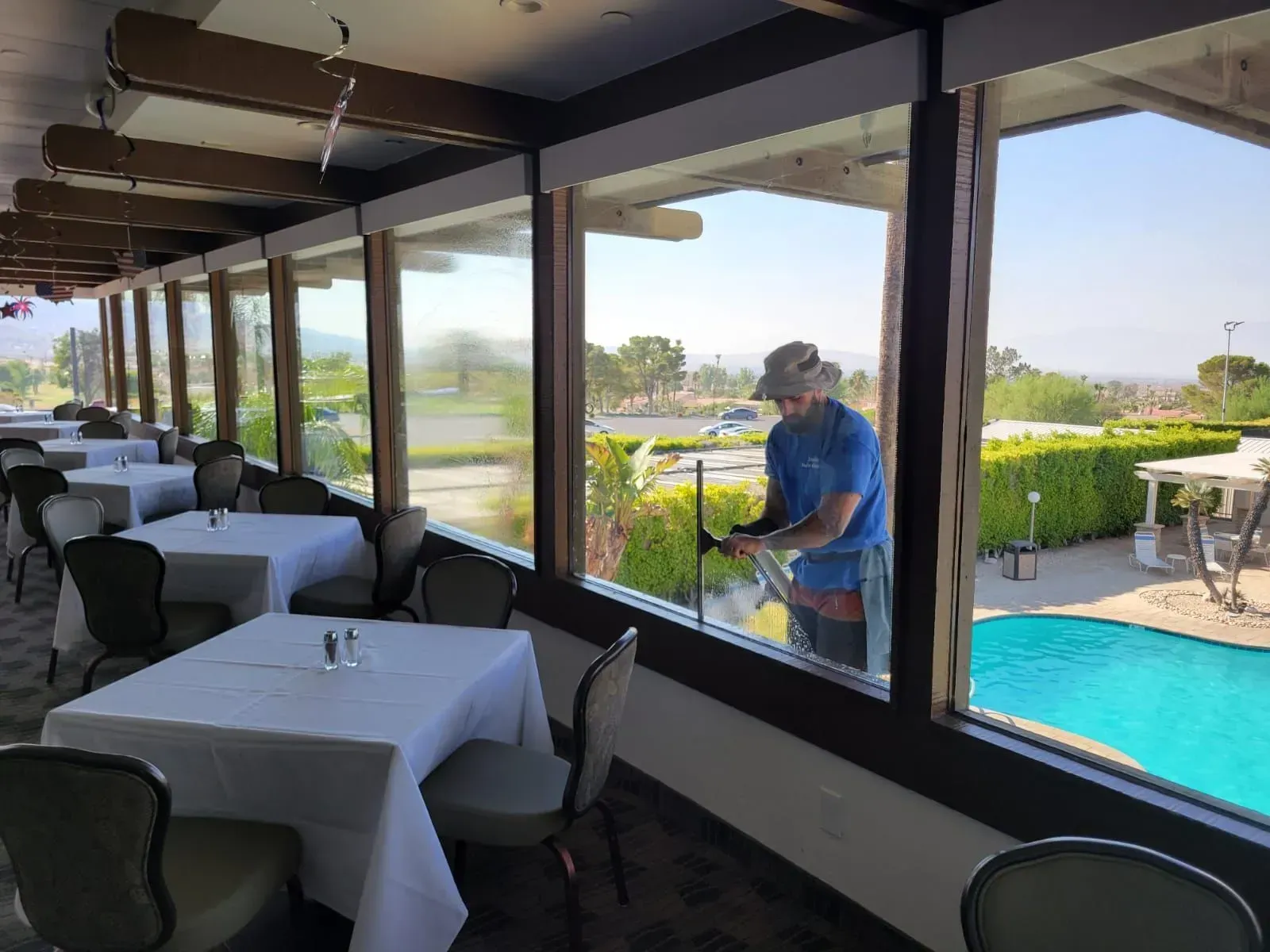 Man cleaning windows in a restaurant with a view of a pool and landscaping.