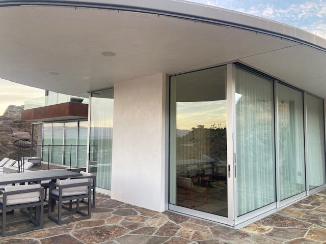 Modern home with large windows, outdoor dining area, mountain view.