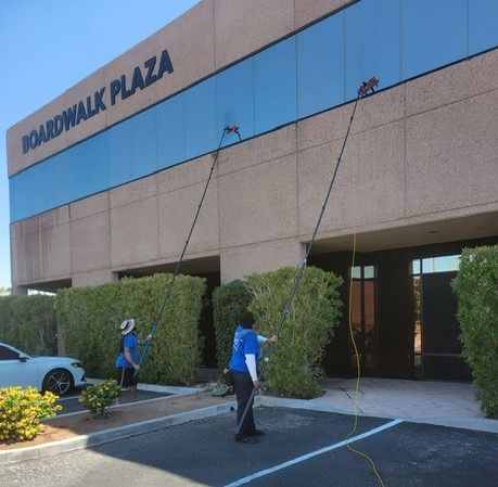 Two window cleaners using long poles to wash windows on a building,