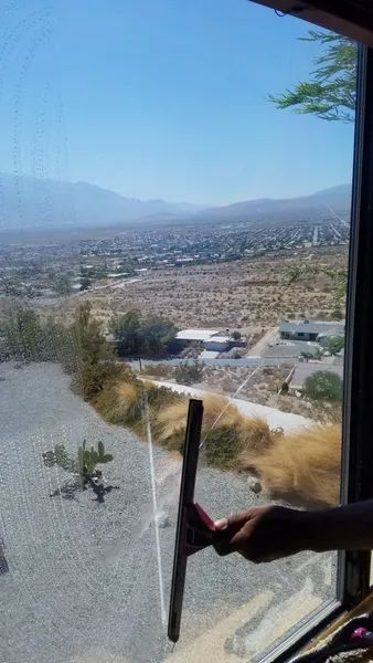 A person cleaning a window with a squeegee, overlooking a desert landscape and mountains.