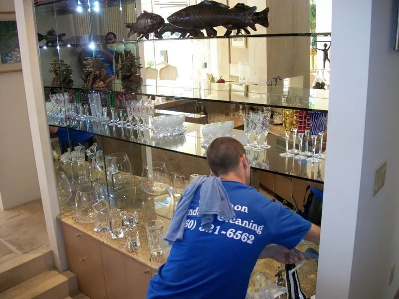 Man cleaning a glass display case filled with glassware, with a light blue shirt, and a phone number.