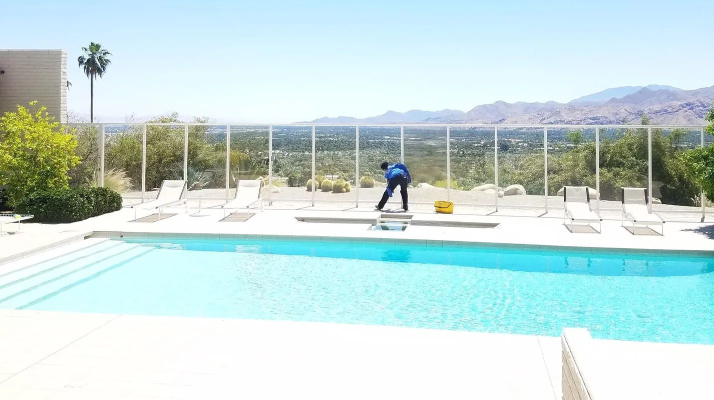 Person cleaning a pool with mountains and blue sky in the background.