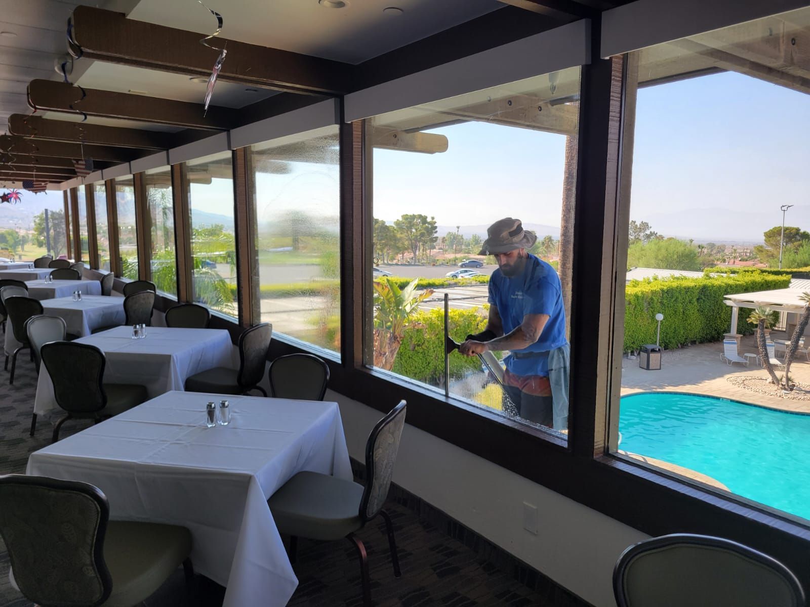 A man is cleaning a window in a restaurant with tables and chairs.