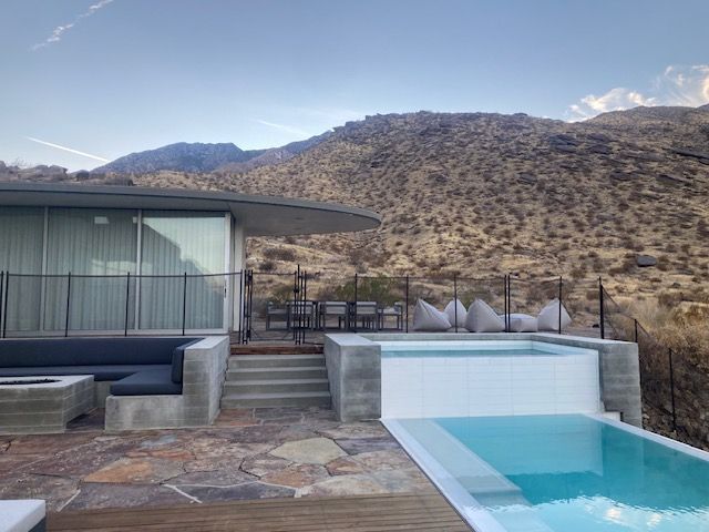 A pool and patio overlook a mountain range. Modern home with outdoor seating and spa.