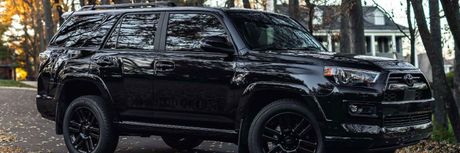 A black suv is parked in a driveway surrounded by trees.