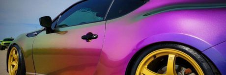 A purple car with yellow wheels is parked on the side of the road.
