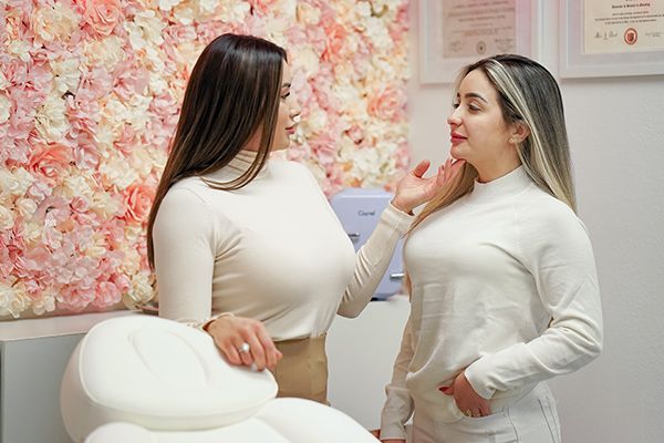 Two women are standing next to each other in front of a wall of flowers.