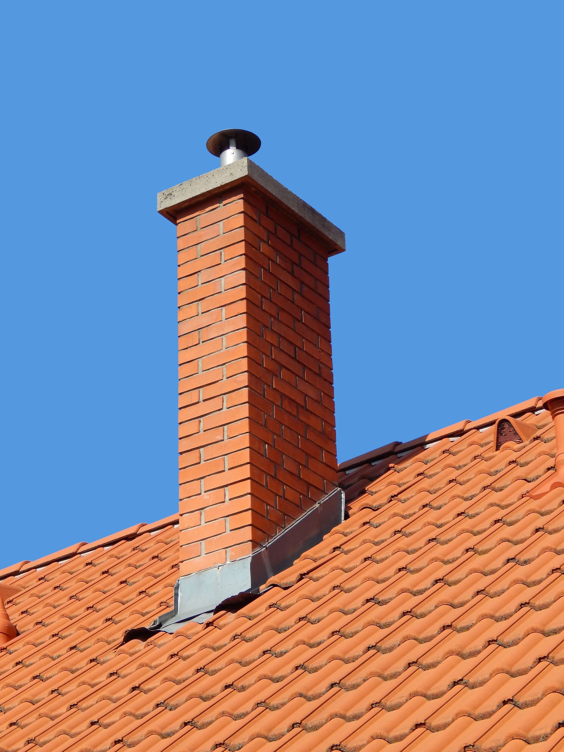 Brick chimney on a red tiled roof against a blue sky.