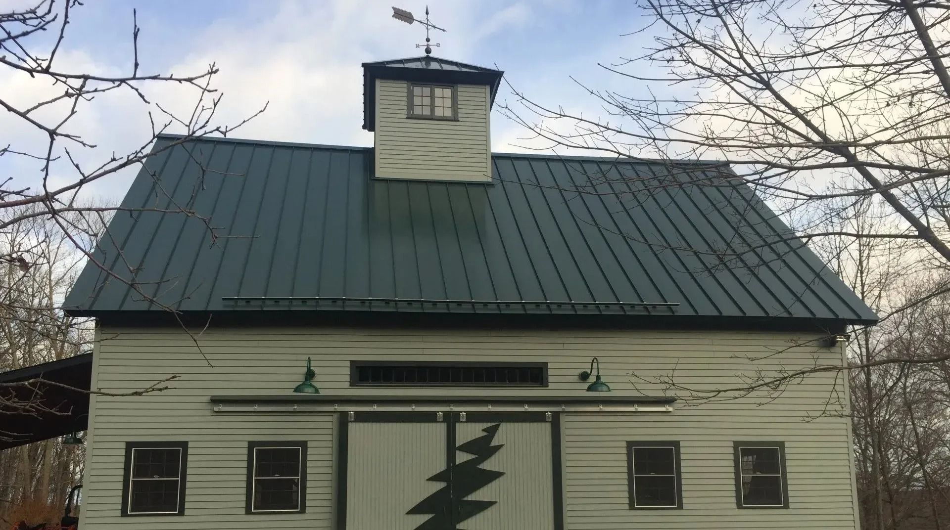 Barn with green metal roof, light-colored siding, cupola, and a decorative tree design on the doors.