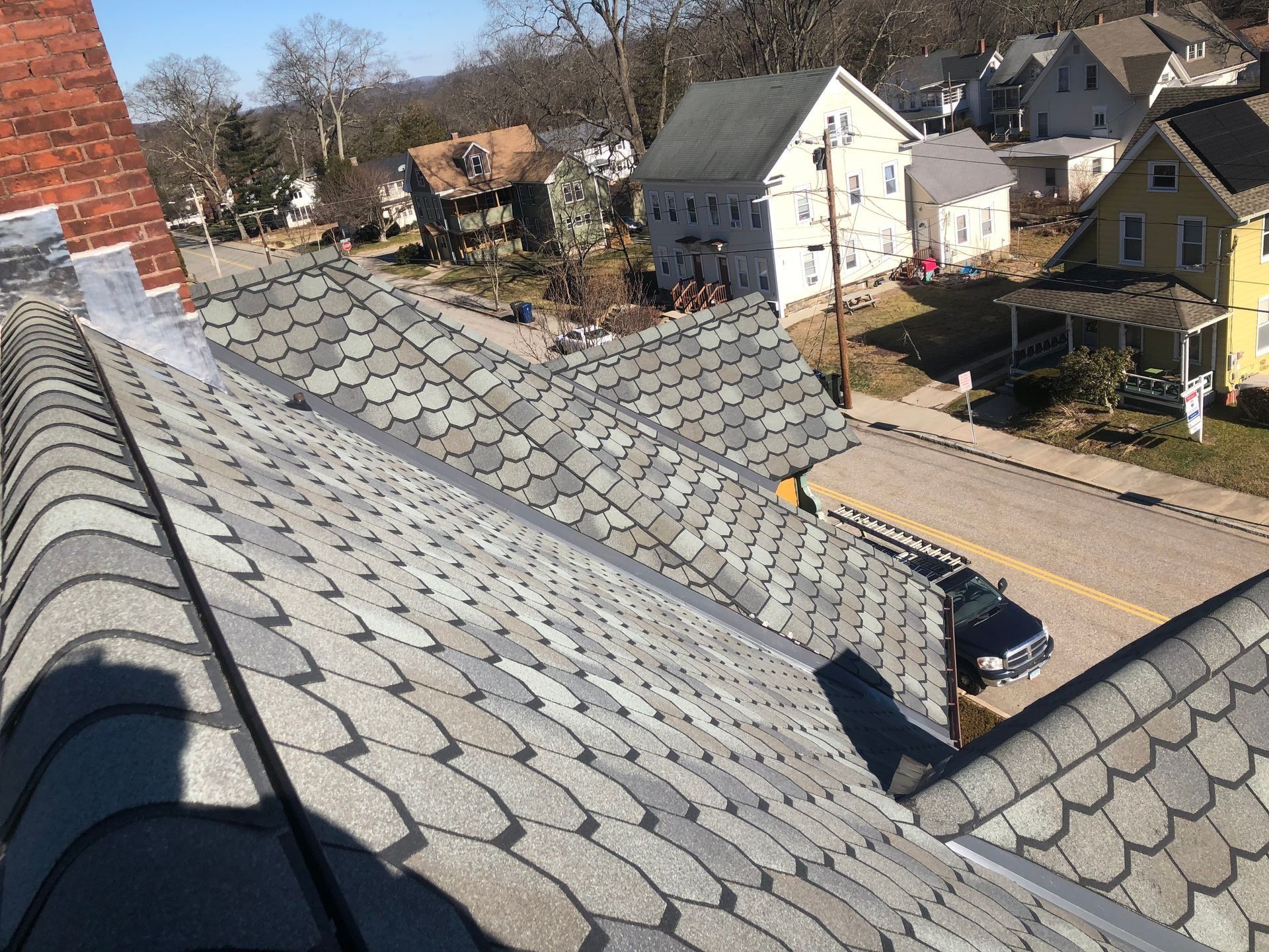 View of rooftops with gray shingles, a street with parked car, and houses.