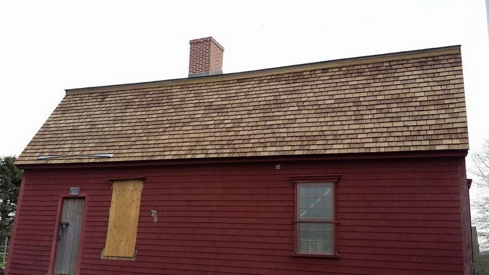 Red, wood-sided building with a brown shingle roof and brick chimney. Windows boarded or missing.