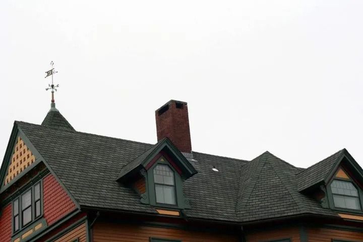 House rooftop with a weathervane, chimney, and dormers under a gray sky.