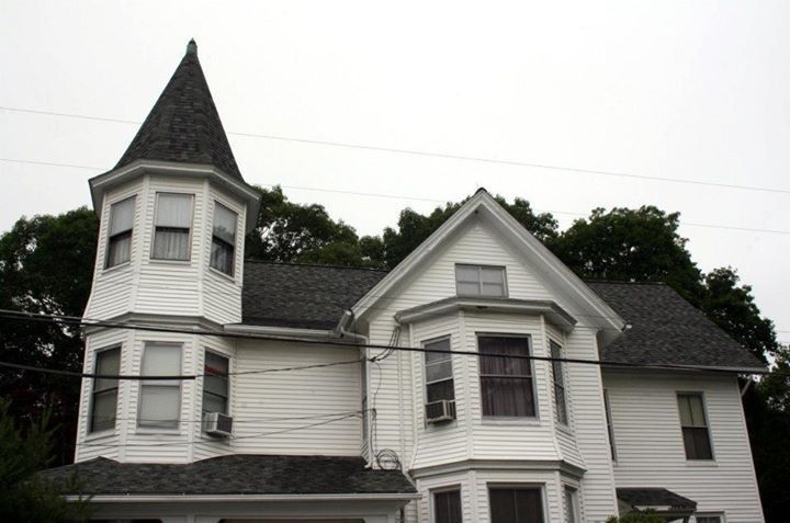 White Victorian house with a turret and dark gray roof.
