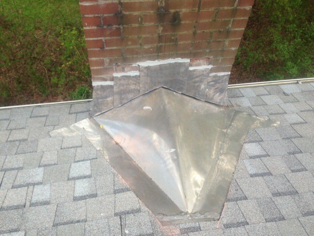 Brick chimney on a shingled roof with metal flashing around the base.