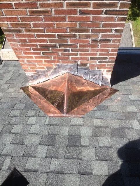 Copper flashing around a brick chimney on a gray shingle roof.