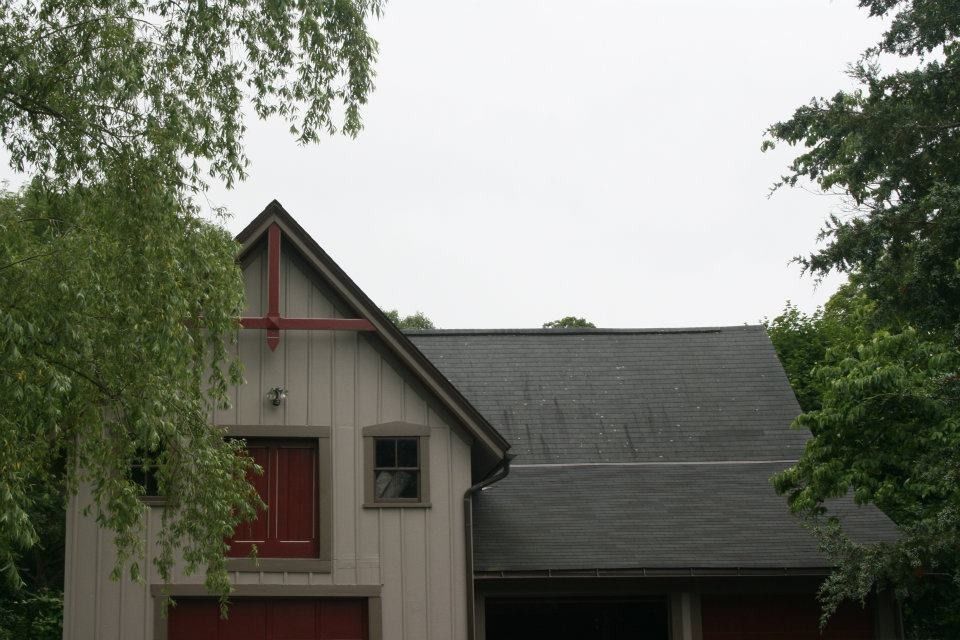 Barn with red doors and trim, framed by green trees against a cloudy sky.