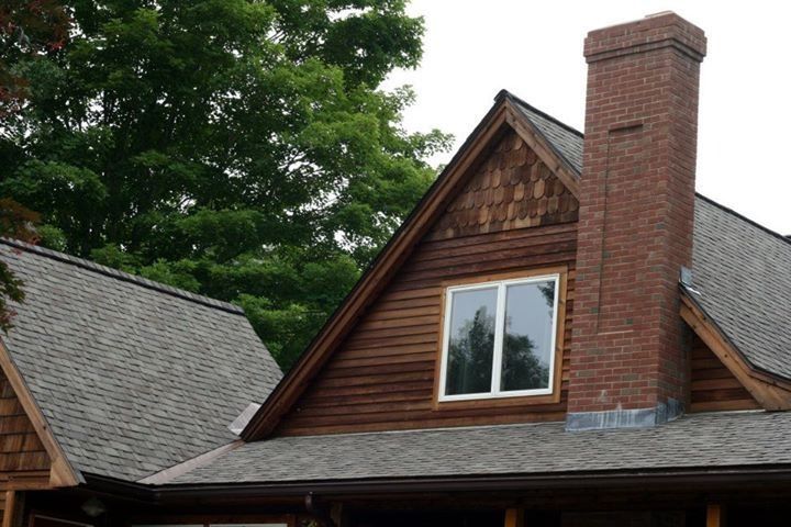 Gabled roof with window, brown siding, brick chimney.