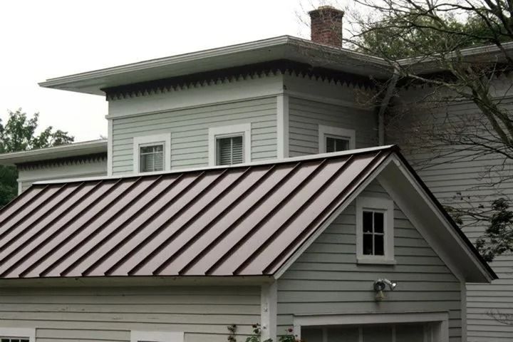 Two-story house with a brown metal roof, gray siding, and a decorative roof edge.