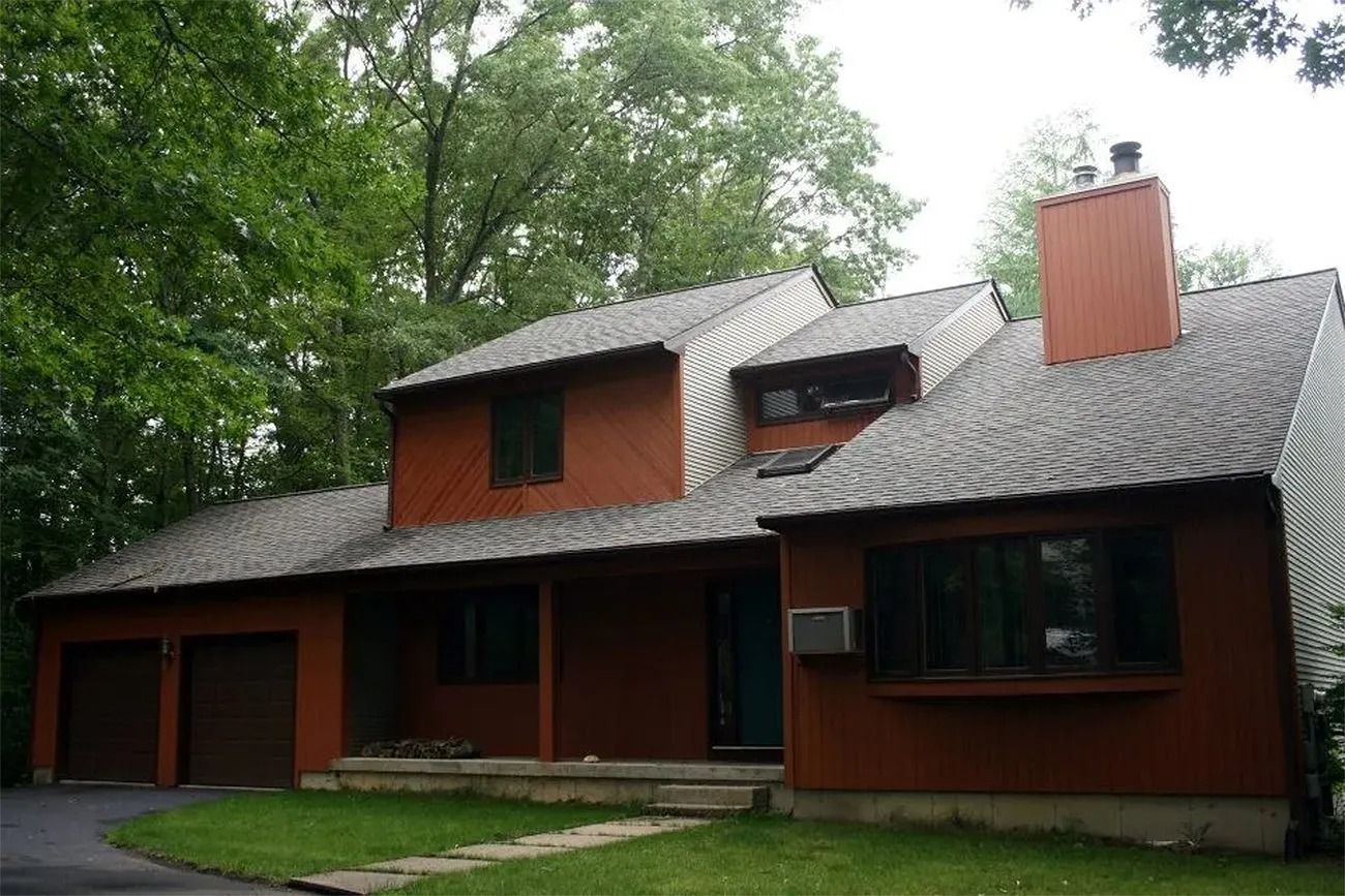 Brown house with gray roof and green trees in the background. Garage and chimney are visible.