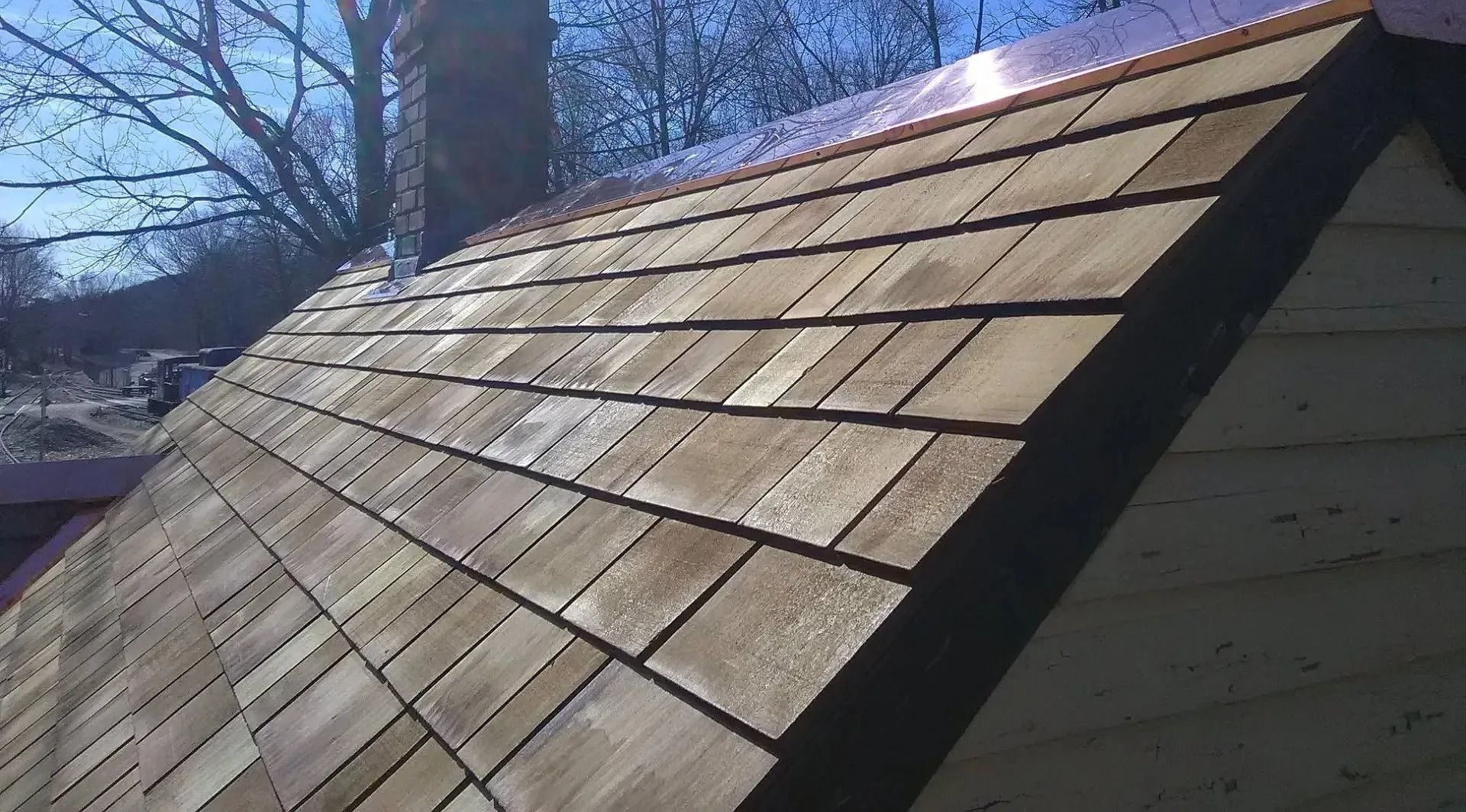 Wooden shingle roof with a copper ridge cap on a sunny day.
