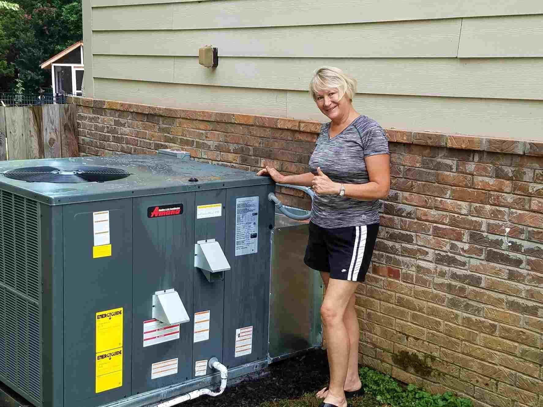 Woman standing beside a large HVAC unit against a brick-and-siding house exterior