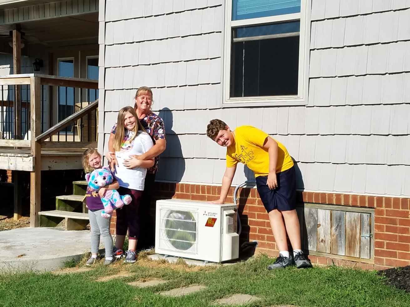 Family standing outside a house beside an air conditioner, with one person leaning over and smiling.