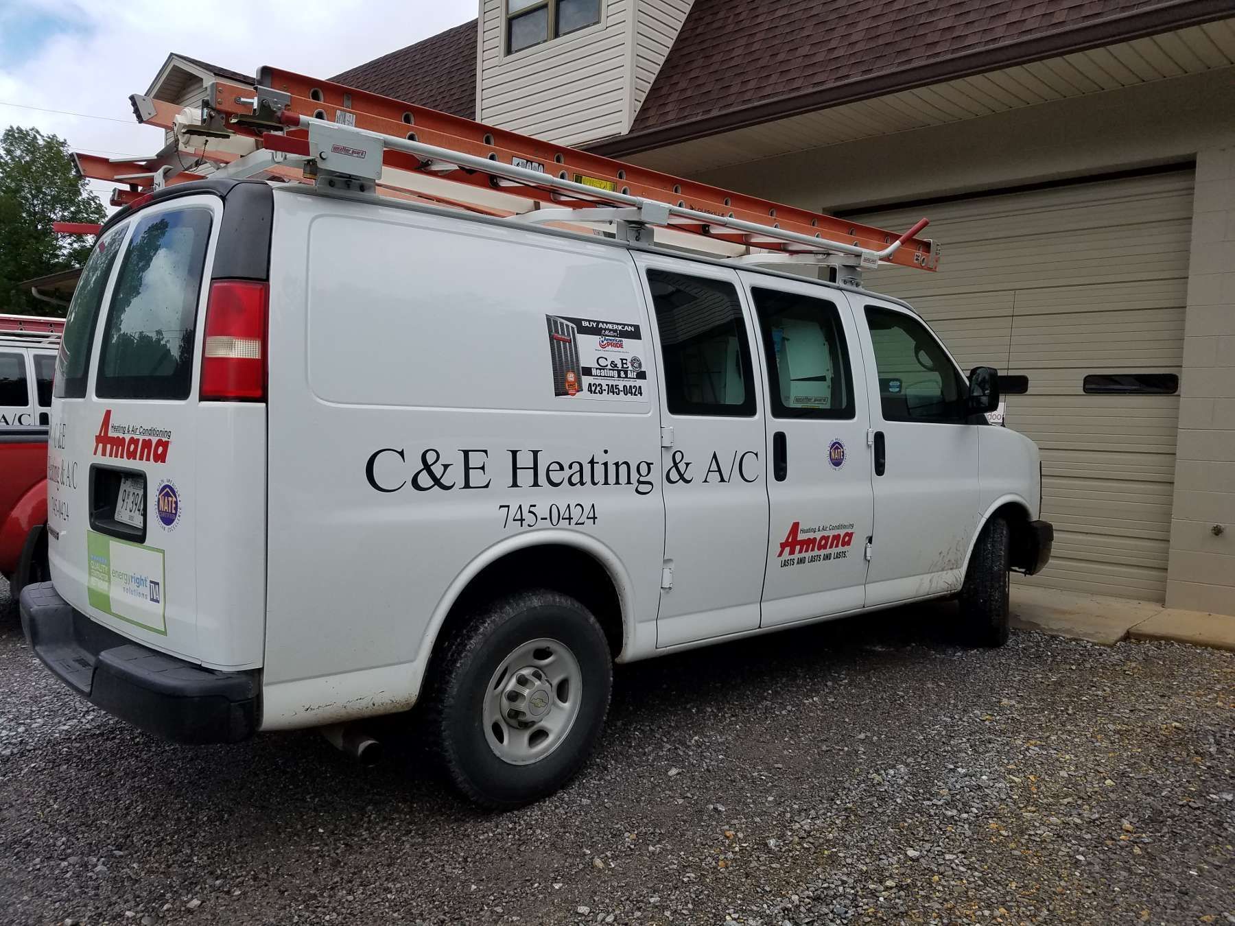 White C&E Heating & A/C work van parked beside a house with ladders on the roof rack
