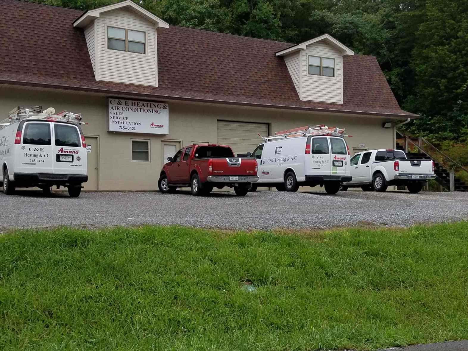 Small building with three parked service vans and a red pickup in front, beside a grassy slope.