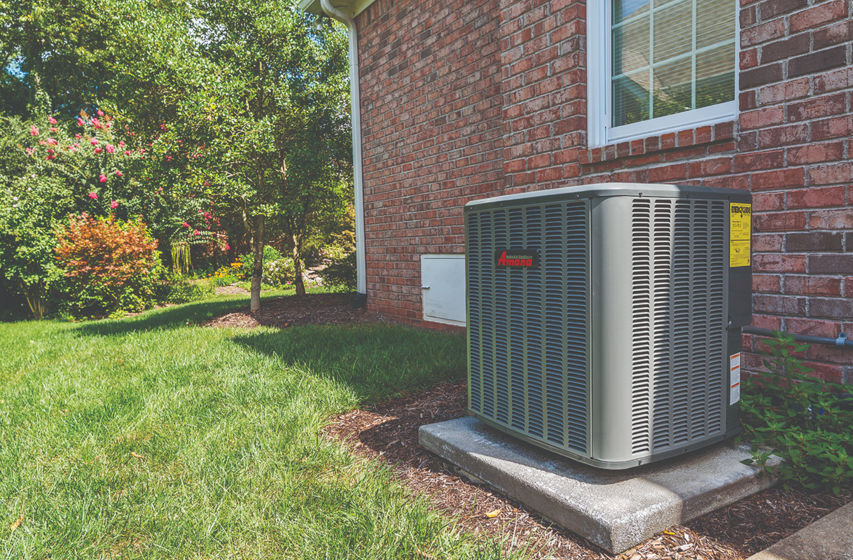 Outdoor air conditioner unit beside a brick house on a grassy lawn