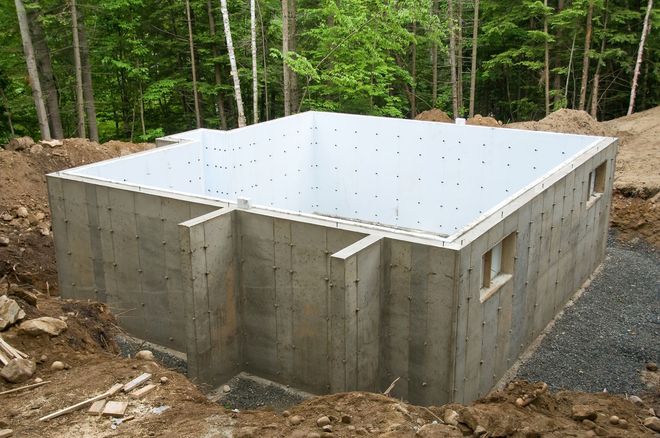 Concrete foundation walls for a house under construction in a wooded area, with a white insulated slab on top.