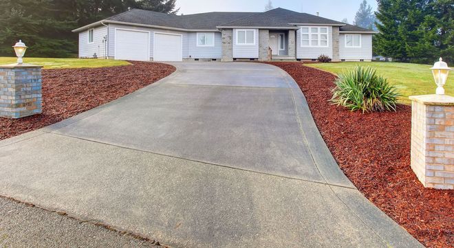 Driveway leading to a white single-story house with red mulch landscaping.