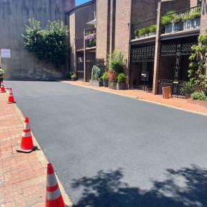 Quiet brick courtyard with newly paved black driveway, orange traffic cones, and potted plants beside buildings